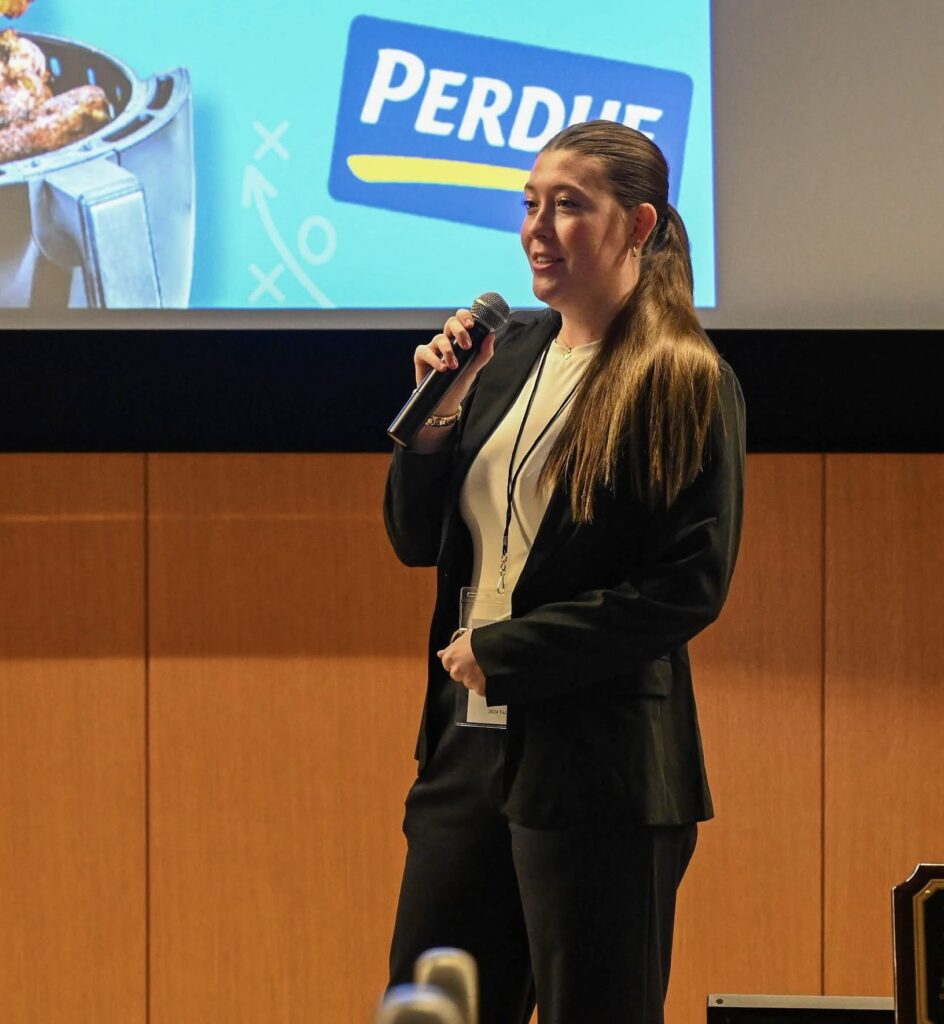 Social Media Marketer, Riley Jones speaks into a microphone during a presentation, competing in ad advertising competition for Perdue.